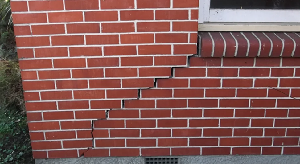 Visible cracking through exterior brick cladding below a window.