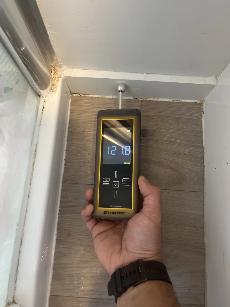 Moisture meter reading being taken near bathroom or wet-area wall finishes.